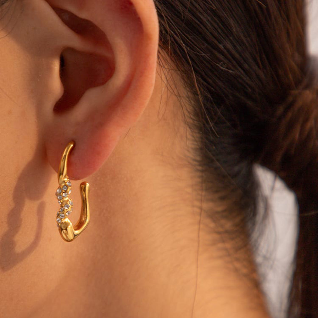 Ein von der Sonne verwöhntes Model zeigt wasserfeste Ohrringe, die mit Zirkonia besetzt sind. Die Ohrringe sind als Goldschmuck und Glitzerschmuck ausgeführt und bestehen aus hochwertigem, langlebigen Edelstahl, der gelb vergoldet ist.